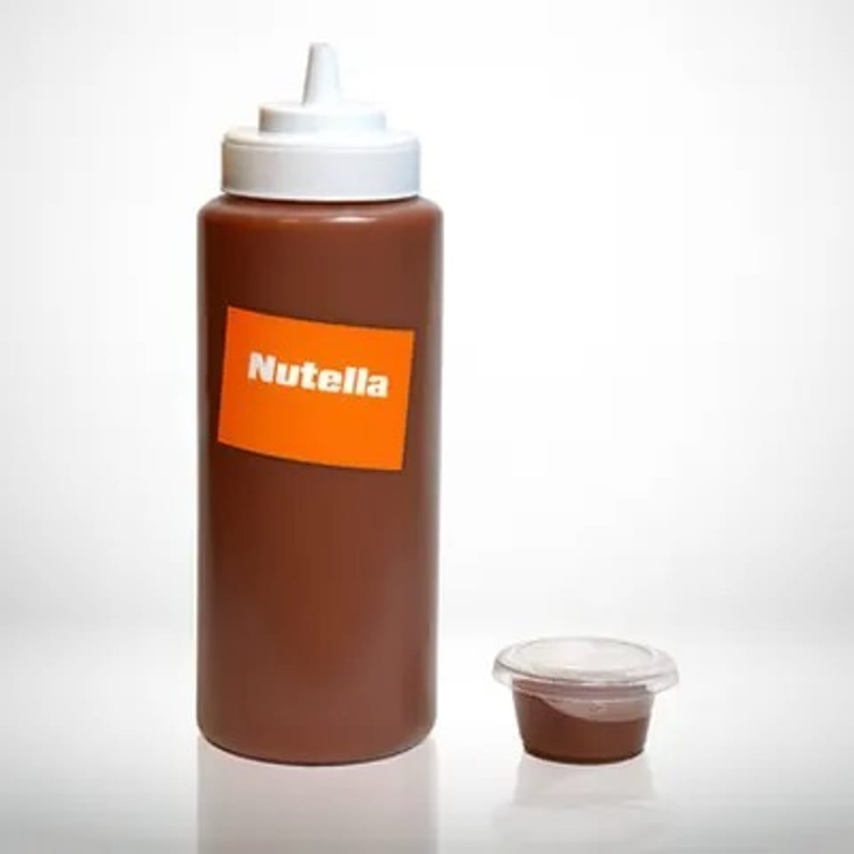 Nutella squeeze bottle filled with chocolate-hazelnut spread beside a small clear dipping cup on a white background.